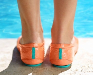 woman wearing coral patent tieks flats by a pool